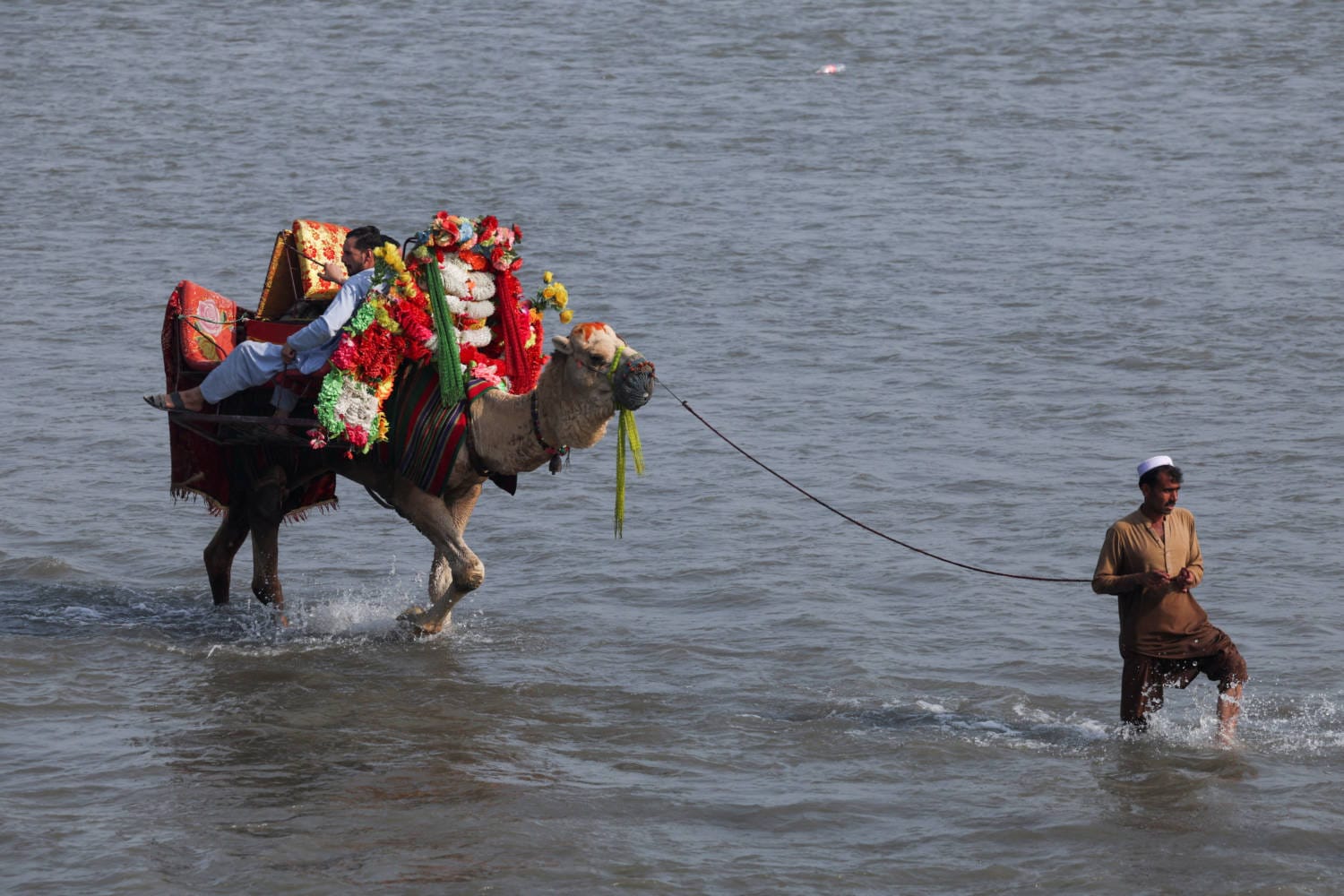 A man leads a camel with men riding on it during the second day of Eid al-Fitr celebrations near Peshawar, Pakistan on April 11, 2024.
